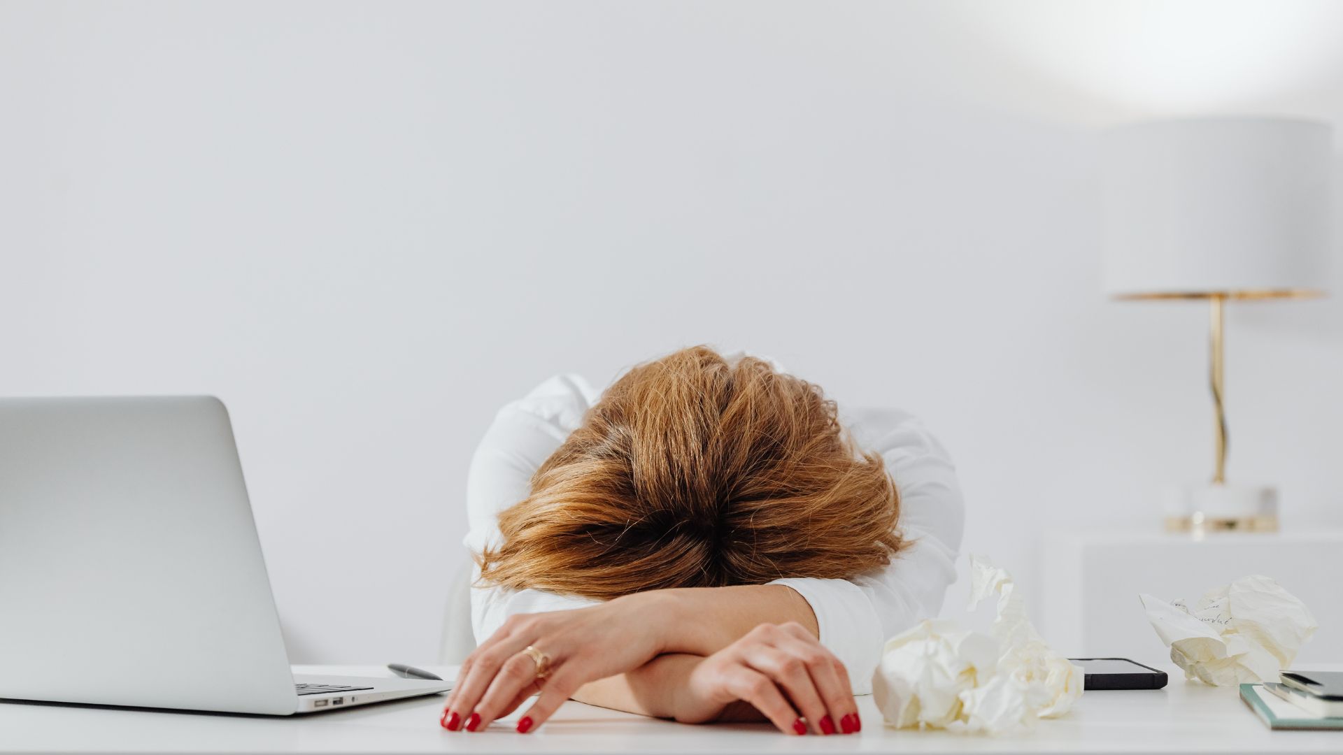 Vrouw met het hoofd op tafel naast een laptop, symbool voor een negatieve mindset op het werk