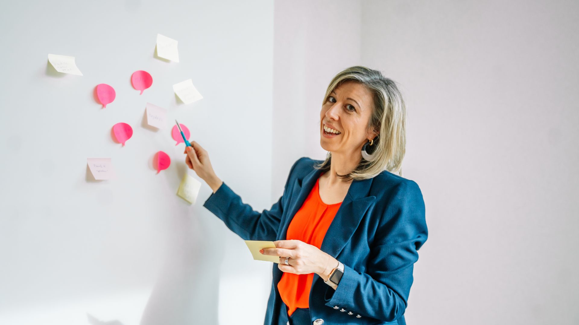 Een trainer wijst naar kleurrijke sticky notes op een whiteboard tijdens een workshop boeiend presenteren