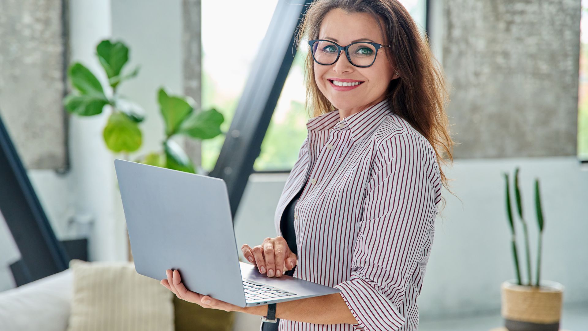 Lachende vrouw met bril achter laptop bij het raam tijdens een online Business Frans-training