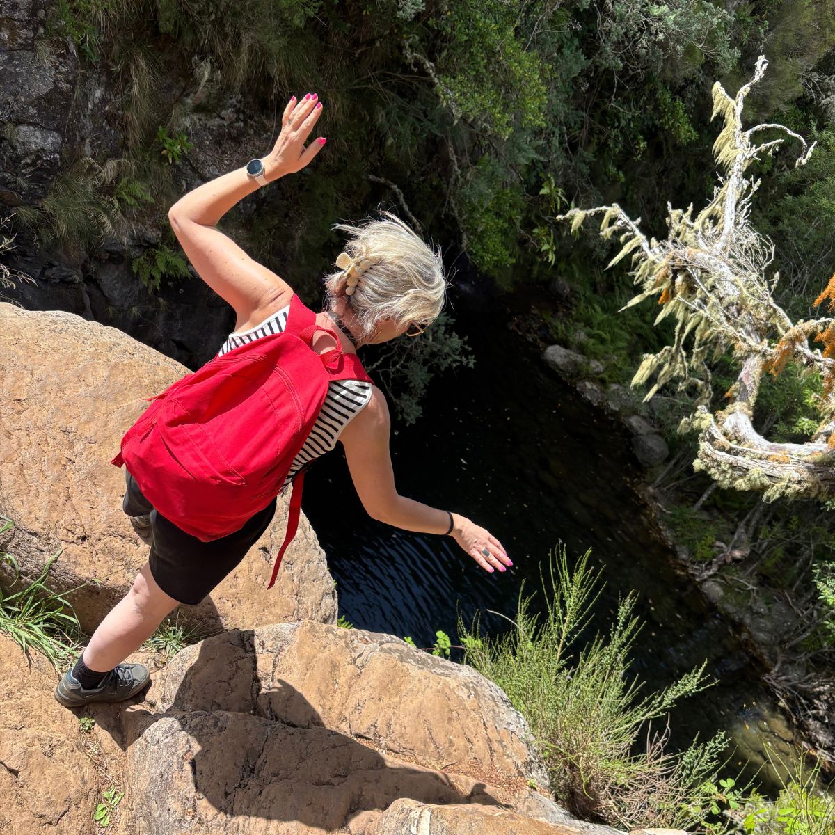 Elke Van Parys met rode rugzak balancerend over rotsen bij een bergstroom op Madeira