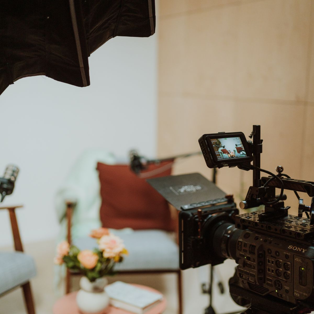 Videocamera op statief met studioverlichting, gericht op een interviewset met stoelen en een rood kussen in de podcaststudio van Studio heydays