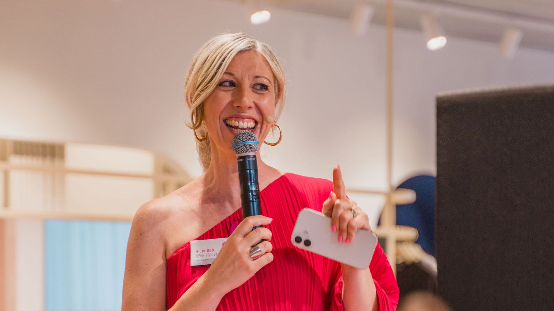 Elke Van Parys spreekt een publiek toe met een microfoon in de hand tijdens een workshop boeiend presenteren