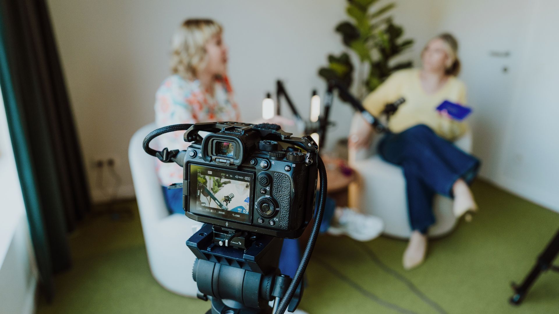 Videocamera op statief gericht op twee vrouwen in gesprek in de podcaststudio van heydays
