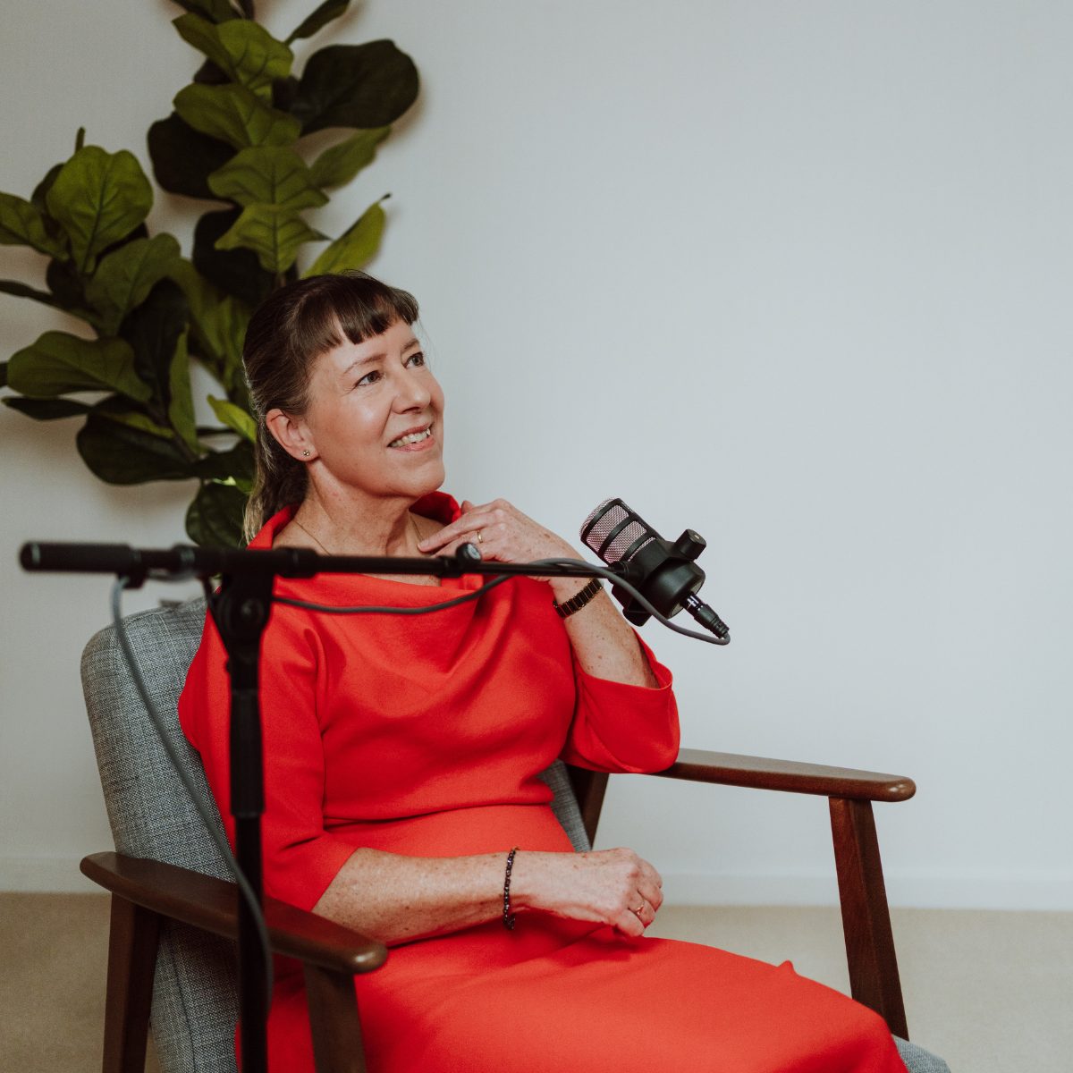 Podcastgaste in rood jasje luistert aandachtig aan de microfoon in de studio
