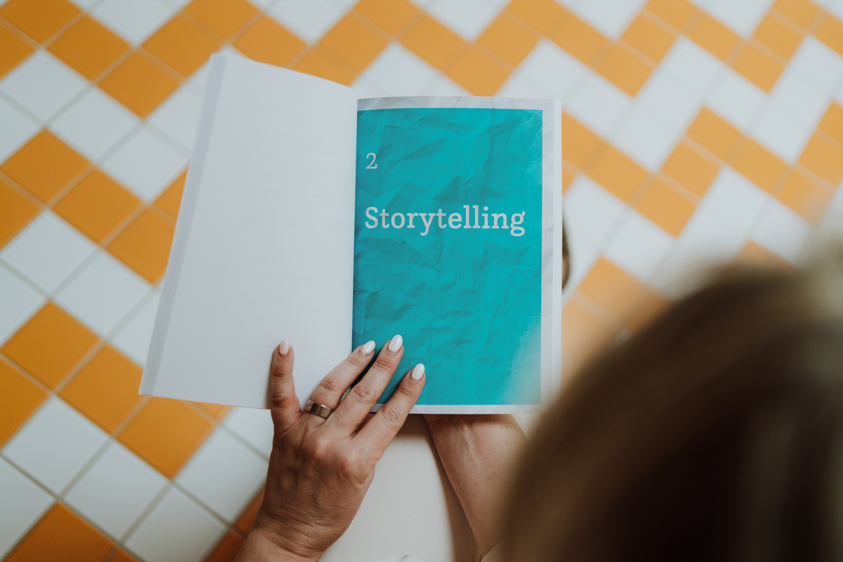 Een persoon houdt een open boek vast met een turquoise pagina getiteld Storytelling